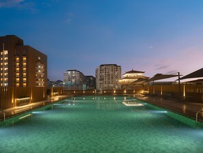 A swimming pool with a tiled floor, surrounded by buildings with illuminated windows and a traditional-style structure with a tiled roof. - Holiday Inn Guilin Qixing by IHG (Guilin)