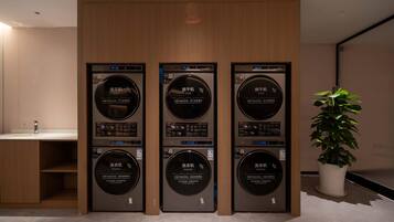 A row of three wall-mounted washing machines with digital displays, a sink, and a potted plant in a modern interior.