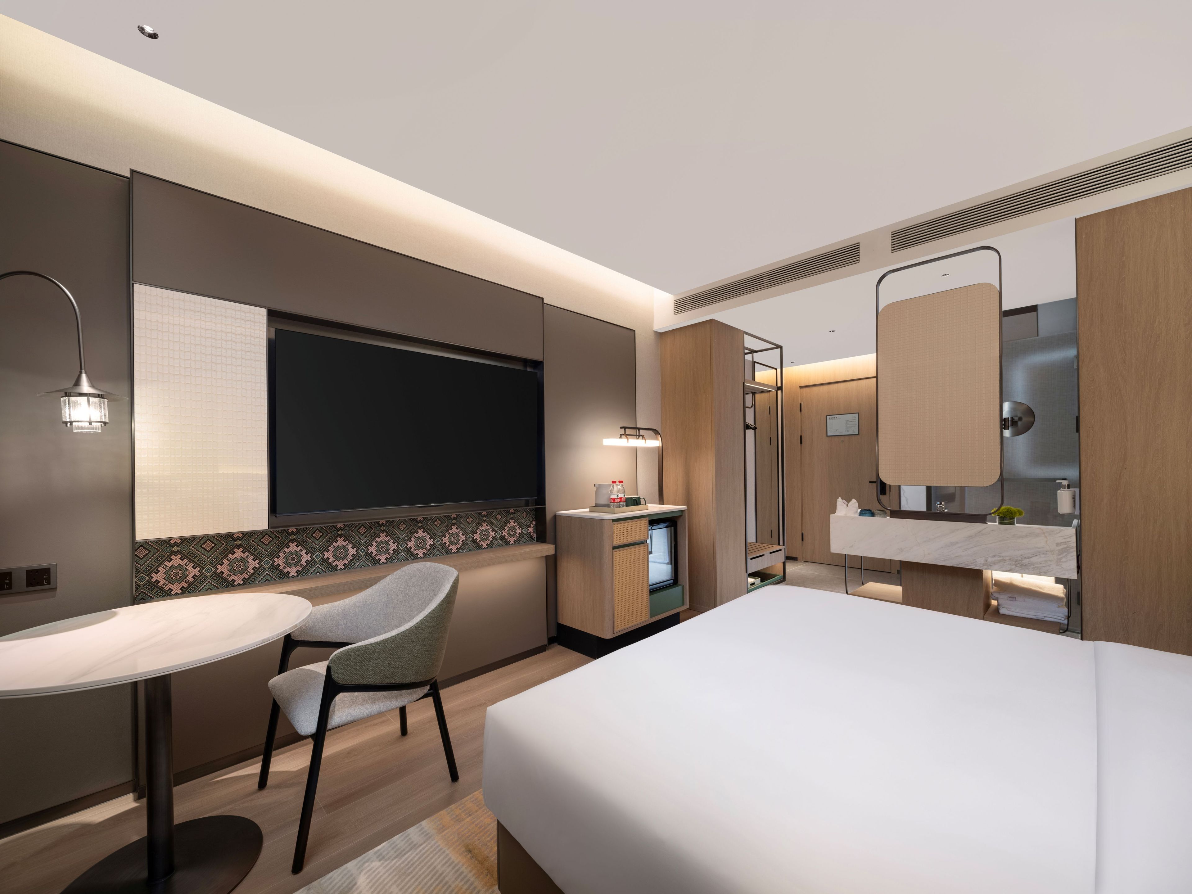 Quarto de hotel moderno com uma cama, uma mesa de trabalho, uma cadeira, toucador com espelho e área de chuveiro.