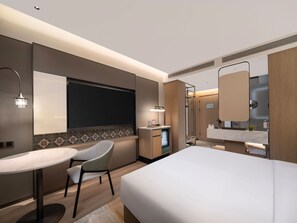 Habitación de hotel moderna con cama, escritorio, silla, tocador con espejo y zona de ducha.