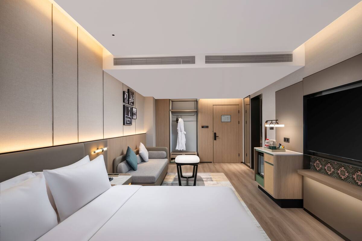 Una habitación de hotel moderna con una cama grande, una zona de estar, un tocador con espejo y un televisor.