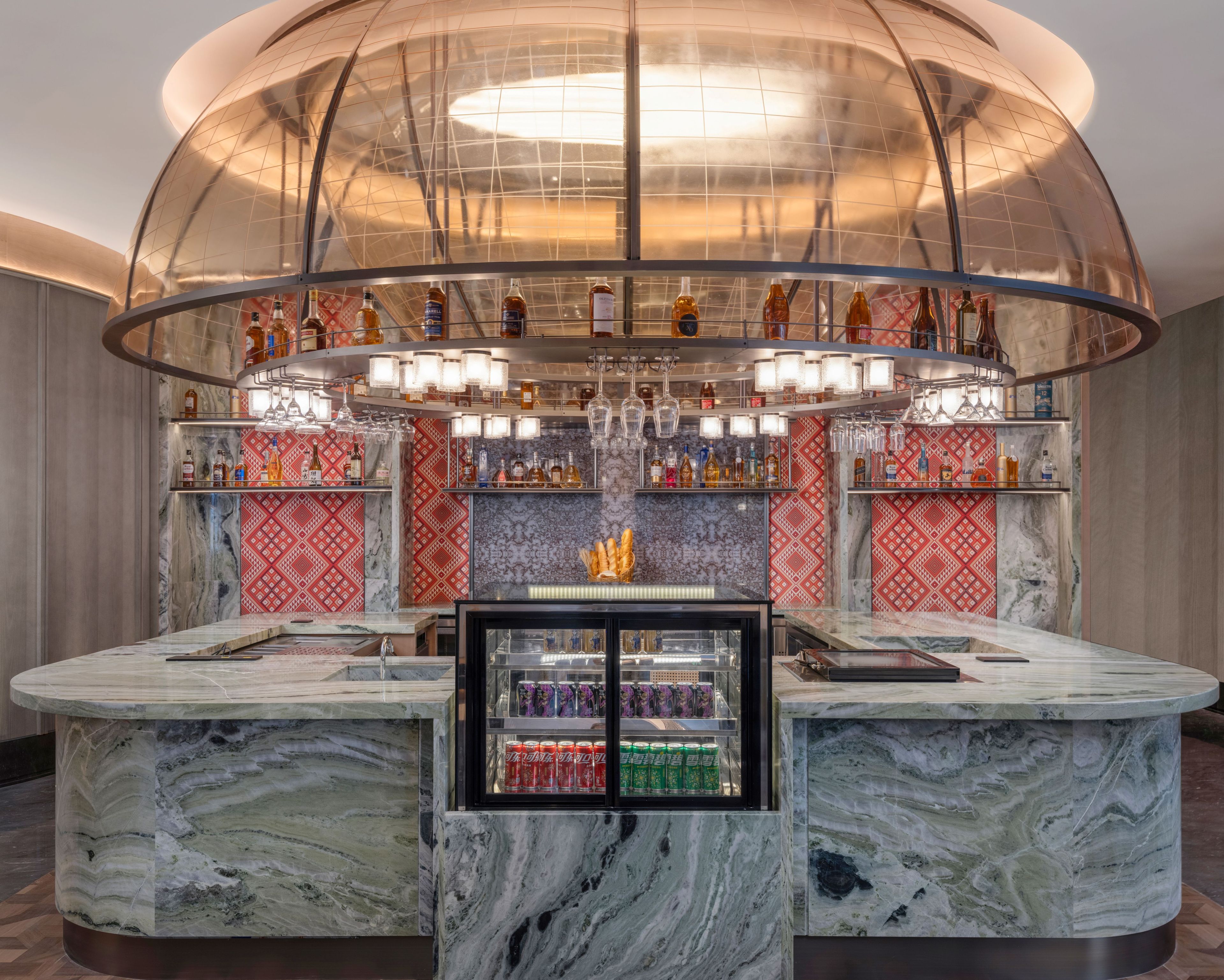 Un espace bar doté d’un comptoir en marbre, d’étagères remplies de bouteilles et d’une vitrine en verre.