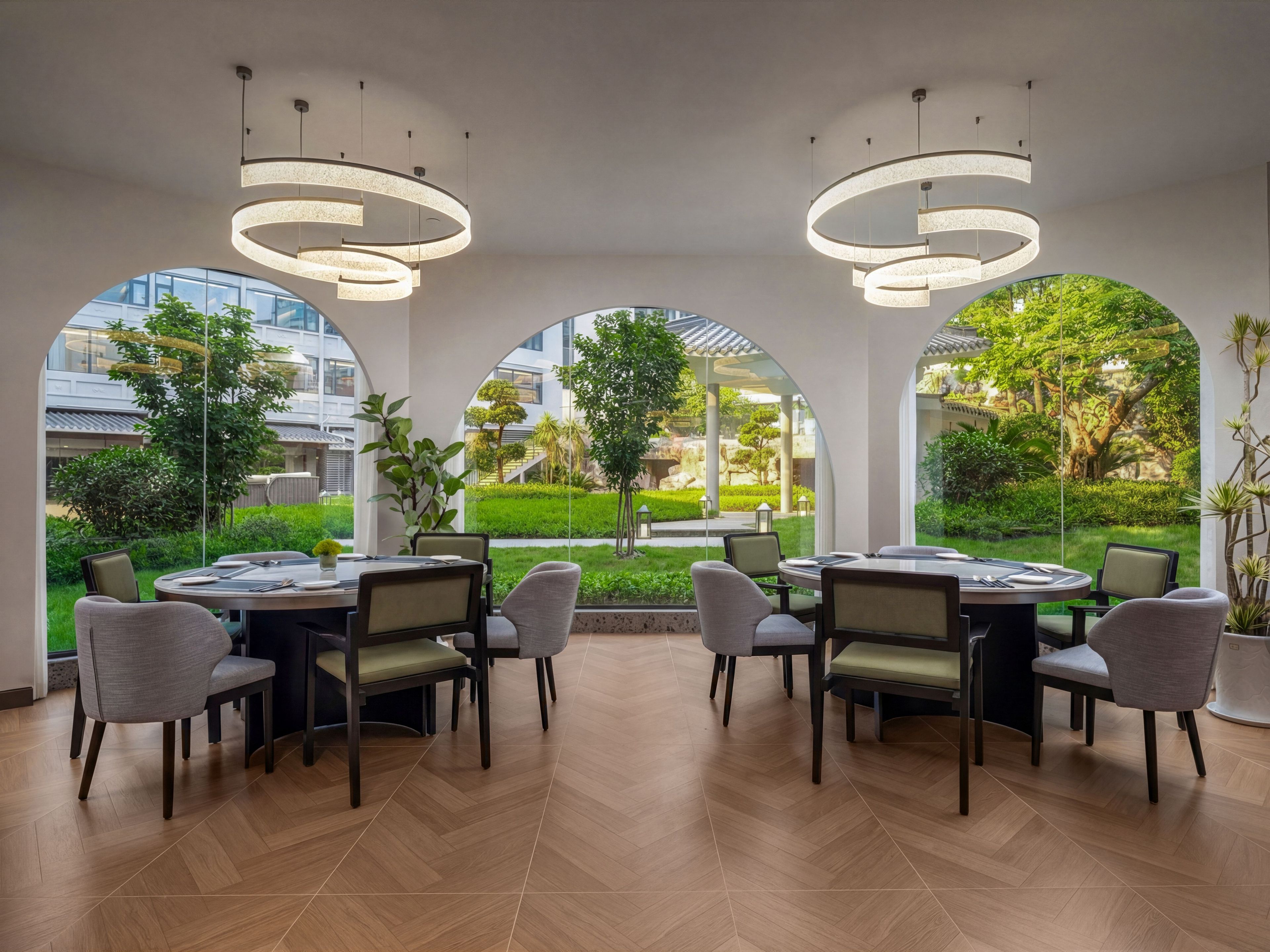 Un espace de restauration moderne, doté de tables et de chaises rondes, de grandes fenêtres en arc et offrant une vue sur un jardin bien entretenu.