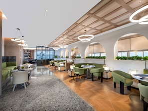 Un hall d’hôtel moderne, aménagé avec différents espaces de détente, un bar et un comptoir d’accueil.