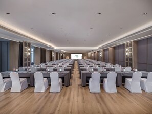 A conference room with rows of tables and chairs, a projector screen at the front, and a wooden floor. - Holiday Inn Guilin Qixing by IHG (Guilin)