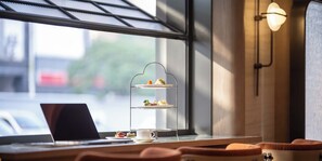 A three-tiered dessert stand with pastries and a laptop on a table near a window.