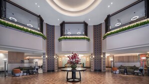 Eine großzügige Lobby mit einem runden Tisch in der Mitte, Sitzbereichen und einer hohen Decke mit runder Beleuchtung.