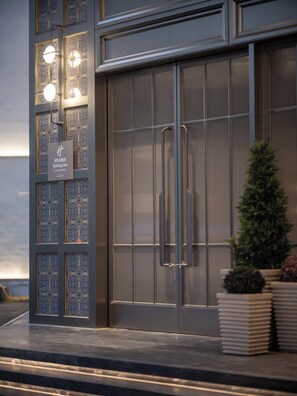 L’entrée d’un hôtel moderne, avec une façade décorative, une enseigne « Holiday Inn » et un petit arbre planté dans un bac.