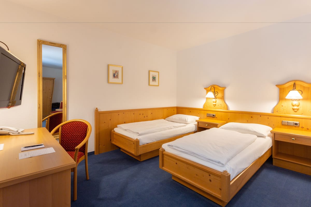 A hotel room with two single beds, a desk with a chair, a mirror, and two bedside lamps.