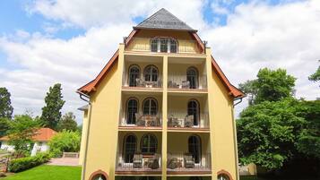 A multi-story building with a yellow facade, multiple balconies, and a red roof.