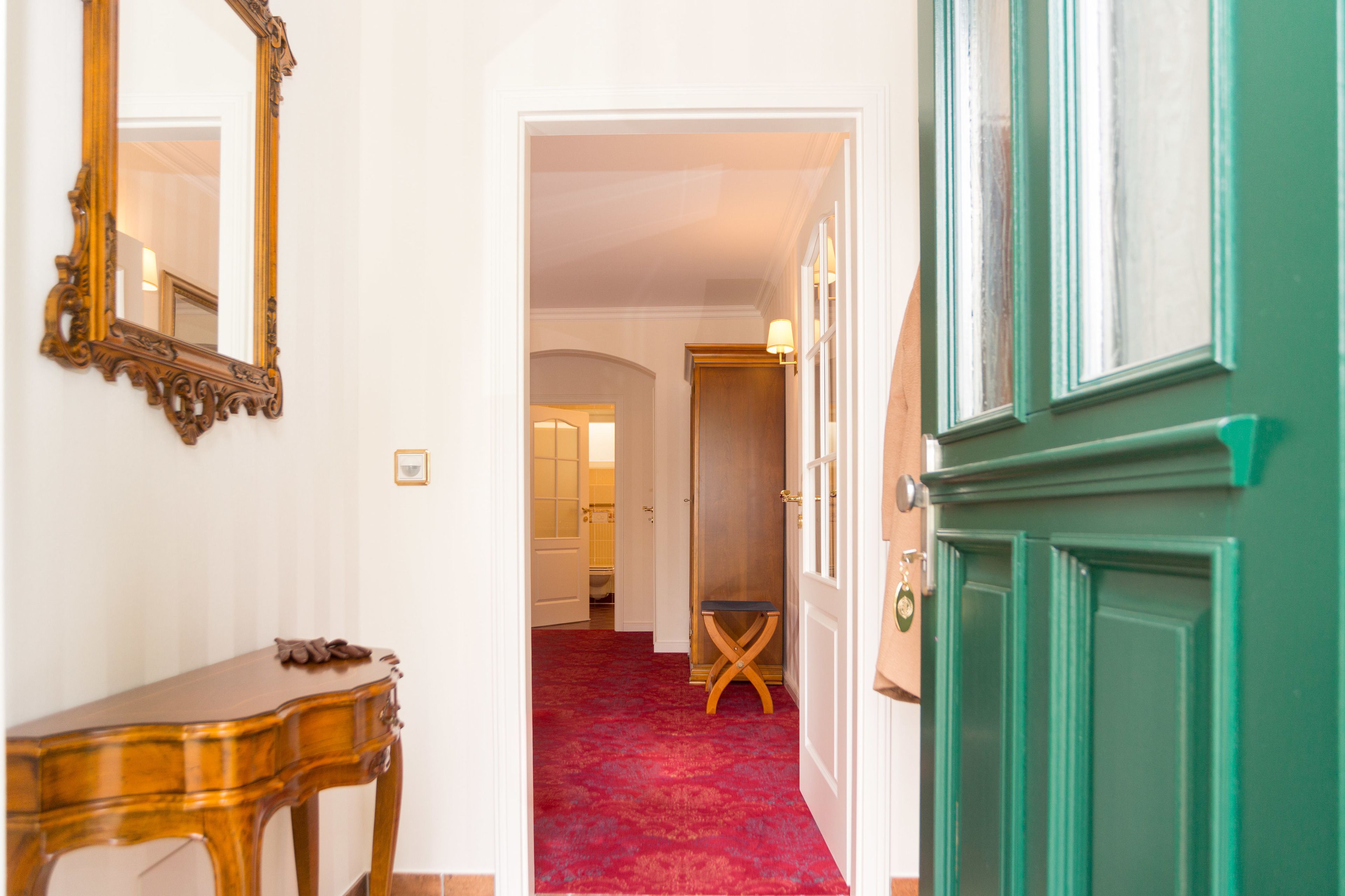 A hallway with a red carpet, a wooden table, a mirror, and a green door.