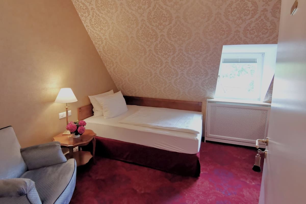 A bedroom with a bed, a nightstand, a lamp, a chair, and a radiator.