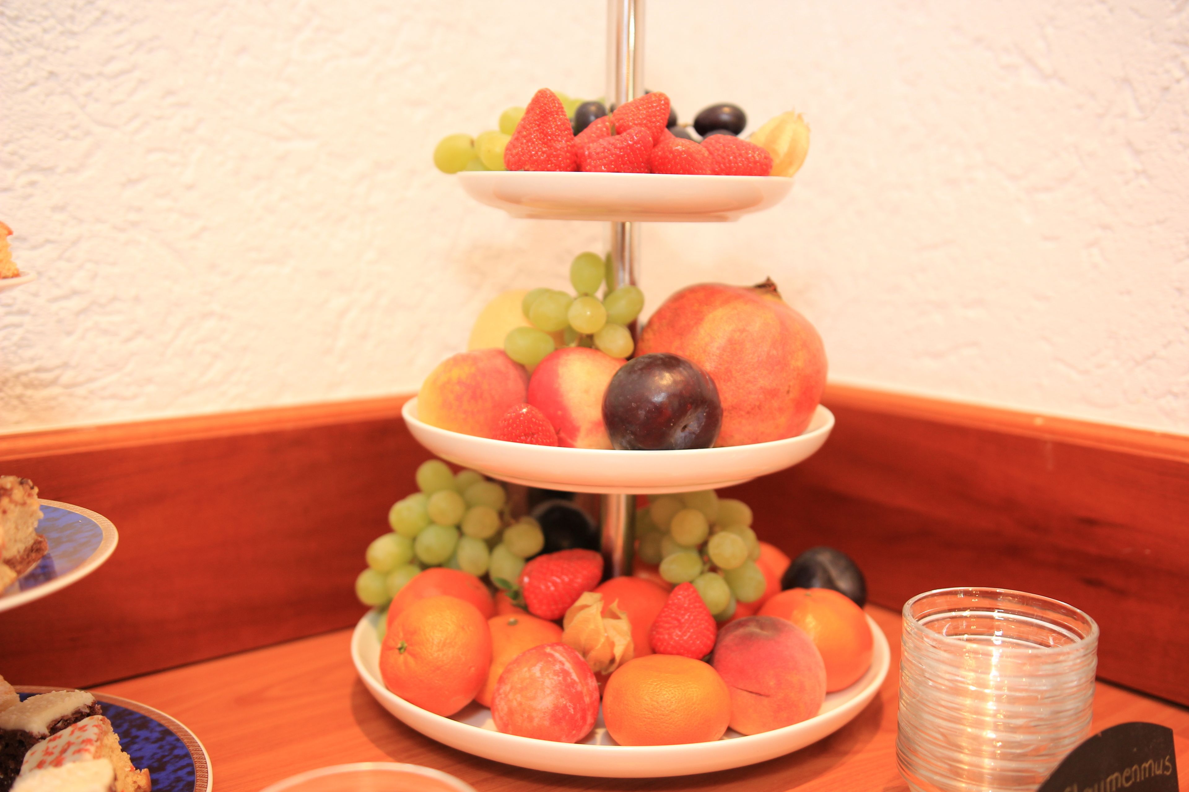 Ein gestaffelter Obststand mit verschiedenen Früchten und einem Glas Wasser auf einem Holztisch.
