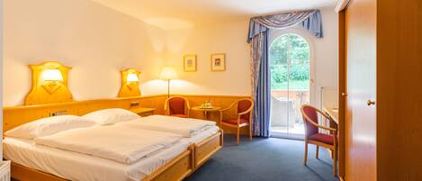 Habitación de hotel con cama doble, dos lámparas de noche, una mesita con una silla y vista al exterior a través de una ventana.