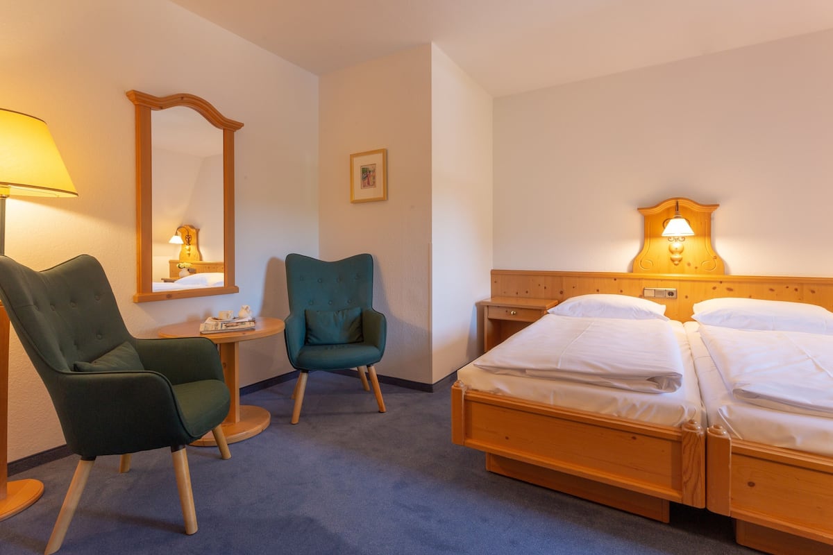 A hotel room with a bed, two chairs, a small table, a mirror, and a wall-mounted lamp.