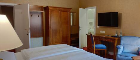 Una habitación de hotel con una cama, un escritorio, una silla, un televisor y un armario.