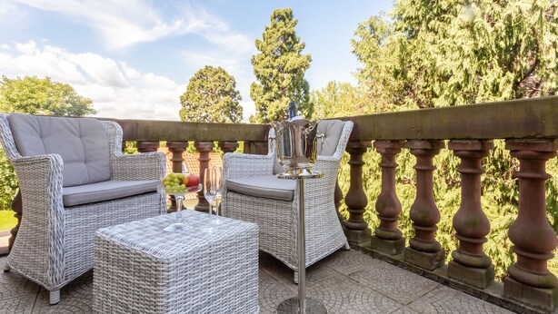 A patio area with wicker furniture, a metal table, and a decorative vase. - Hotel Erbprinzenpalais (Wernigerode)