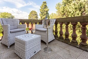 Un espace patio aménagé avec des meubles en osier, une table en métal et un vase décoratif.