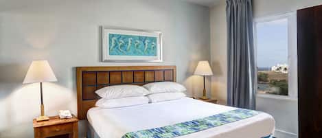 A hotel room with a large bed, two bedside lamps, a wooden headboard, a framed artwork above the bed, and a view of the outdoors through a window.