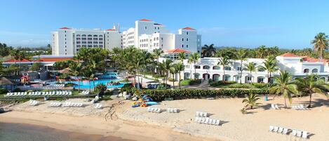 A beachfront hotel with multiple buildings, a pool area, and several palm trees.