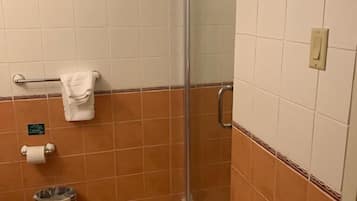Une petite salle de bain avec une douche, des toilettes et une poubelle.