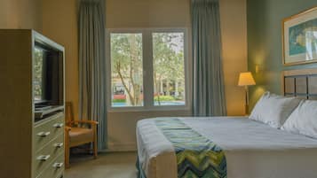 Una habitación de hotel con cama, televisión, silla, ventana con cortinas y lámpara.