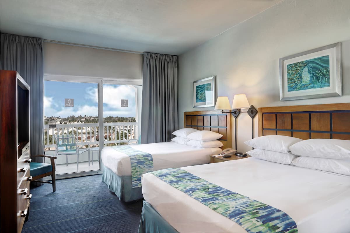 Habitación de hotel con dos camas, una silla, un televisor y un balcón con vistas.