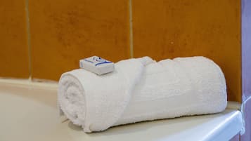 Una toalla blanca enrollada con una etiqueta azul y blanca sobre una superficie blanca, frente a una pared de azulejos.