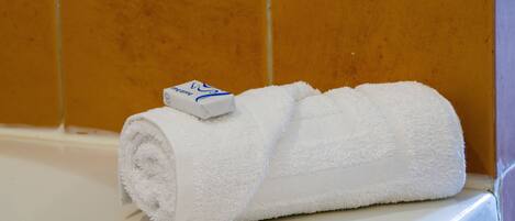 A white towel rolled up with a blue and white tag on a white surface against a tiled wall.