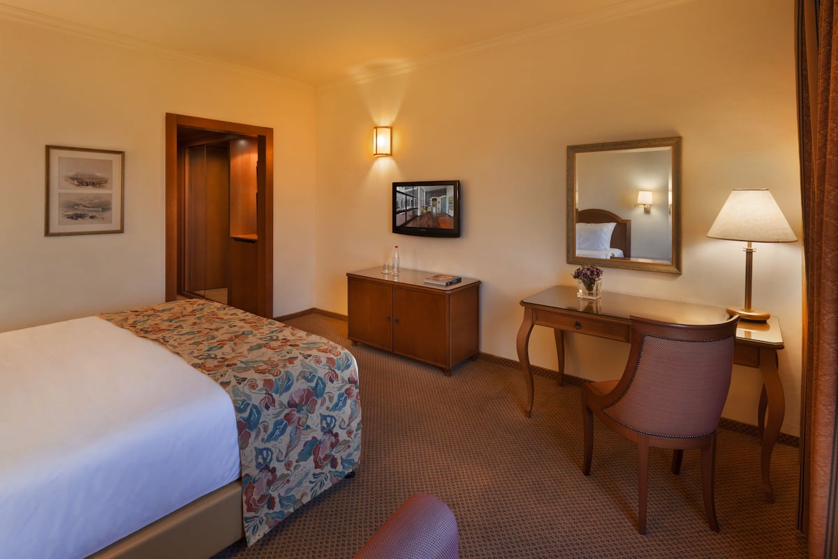 Habitación de hotel con cama, escritorio, silla, cómoda, espejo y lámpara.
