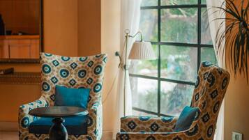 A room with two patterned armchairs, a small round table, and a large window with curtains.