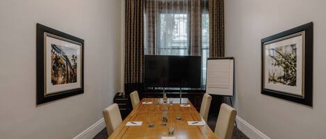 A conference room with a long table, chairs, a projector screen, and framed pictures on the walls.