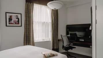 Habitación de hotel con cama, escritorio con computadora, silla, televisor y ventana con cortinas.