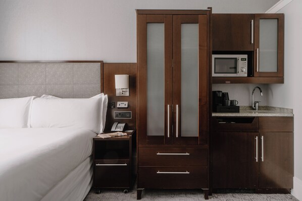 A hotel room with a bed, a wardrobe with a microwave, a nightstand, and a small kitchenette. - The Grand at Trafalgar Square (London)