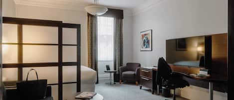 A hotel room with a sofa, a desk, a chair, a TV, and a window with curtains.