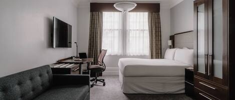 Habitación de hotel con cama, escritorio con silla, sofá, armario y televisor en la pared.