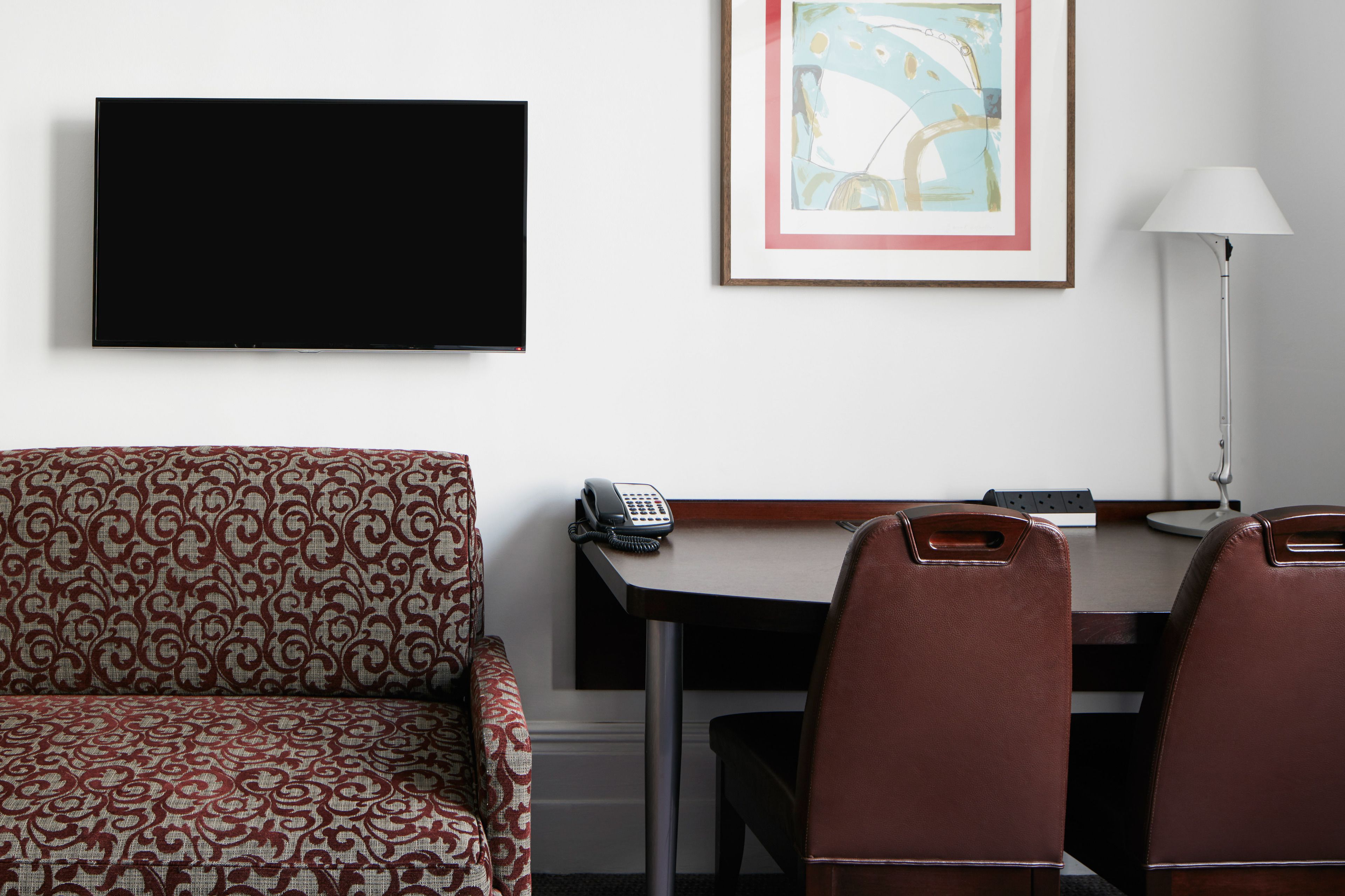 Ein Hotelzimmer mit einer Couch, einem Schreibtisch mit Telefon, einer Lampe und einem gerahmten abstrakten Gemälde.