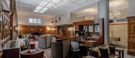 A spacious lobby with a high ceiling, ornate wood paneling, and a central seating area with multiple chairs and a sofa.