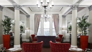 A lobby with red patterned chairs, a chandelier, and large windows with curtains. - The Grand at Trafalgar Square (London)