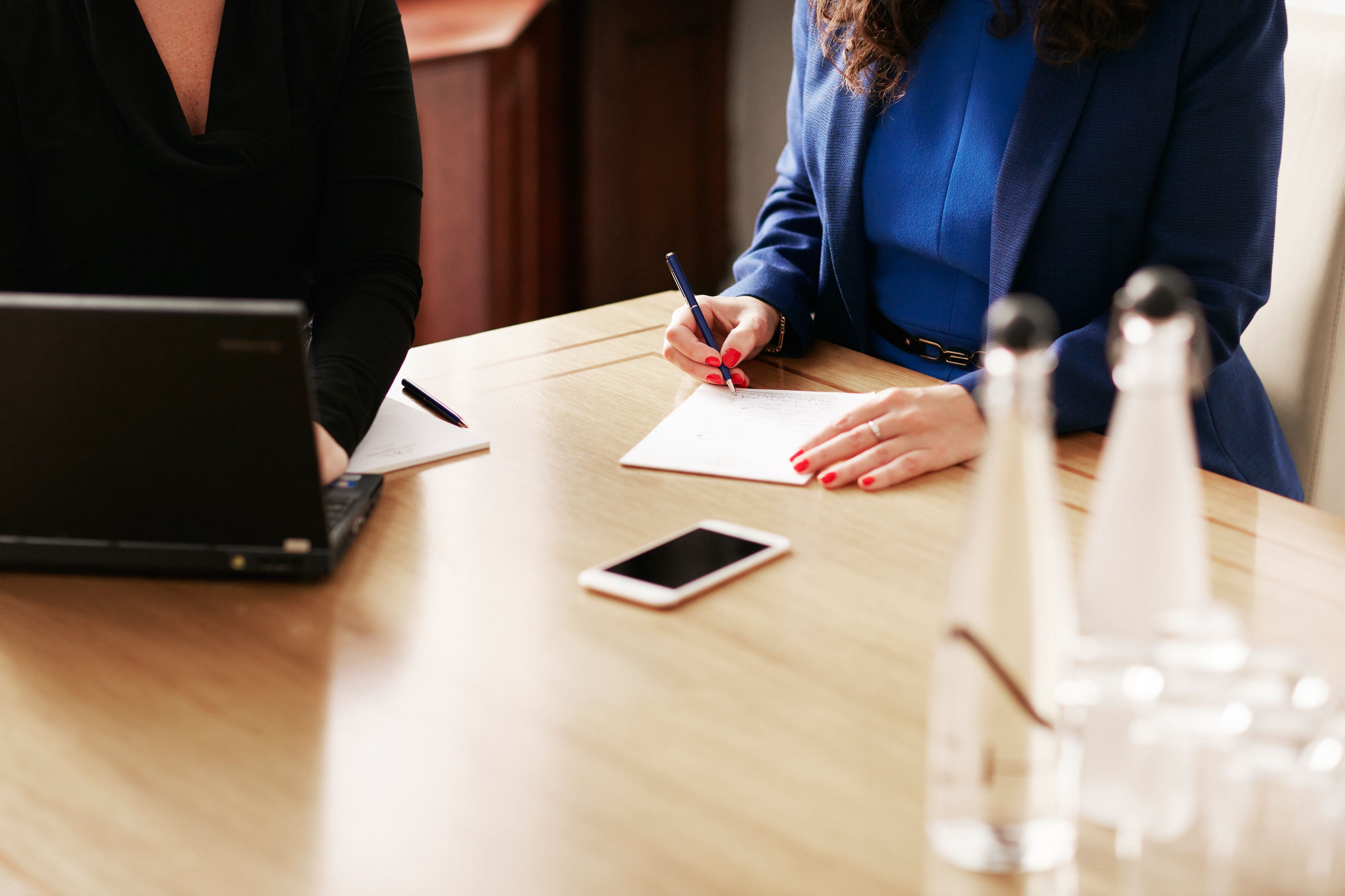 A wooden table with a laptop, a smartphone, and documents.