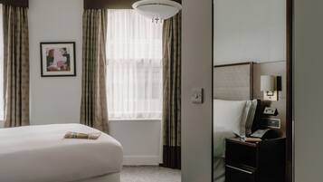 Habitación de hotel con cama, mesita de noche con lámpara, ventana con cortinas y un cuadro en la pared.