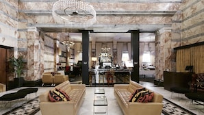 A spacious lobby with marble walls, a bar area, and seating arrangements. - The Grand at Trafalgar Square (London)