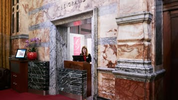 A marble reception desk with a sign reading "THE GRAND" and a red carpet leading to the entrance.