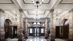 A grand lobby with marble columns, a red carpet, and a chandelier. - The Grand at Trafalgar Square (London)