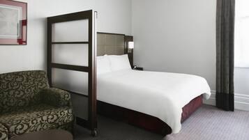 Ein Hotelzimmer mit Bett, Sofa, kleinem Tisch und einem Fenster mit Vorhängen.