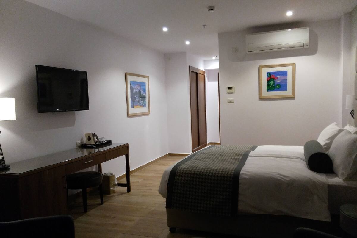 Une chambre d’hôtel avec un lit, un bureau, une chaise, une télévision et des tableaux encadrés au mur.