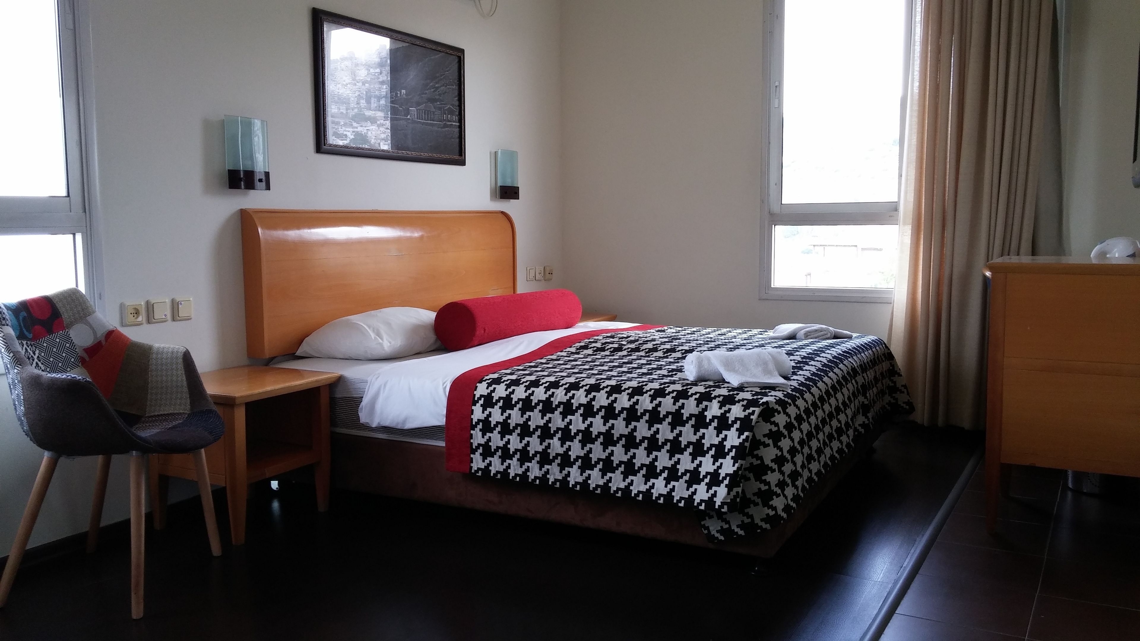 Une chambre d’hôtel avec un lit en bois, une chaise, une petite table et une commode.