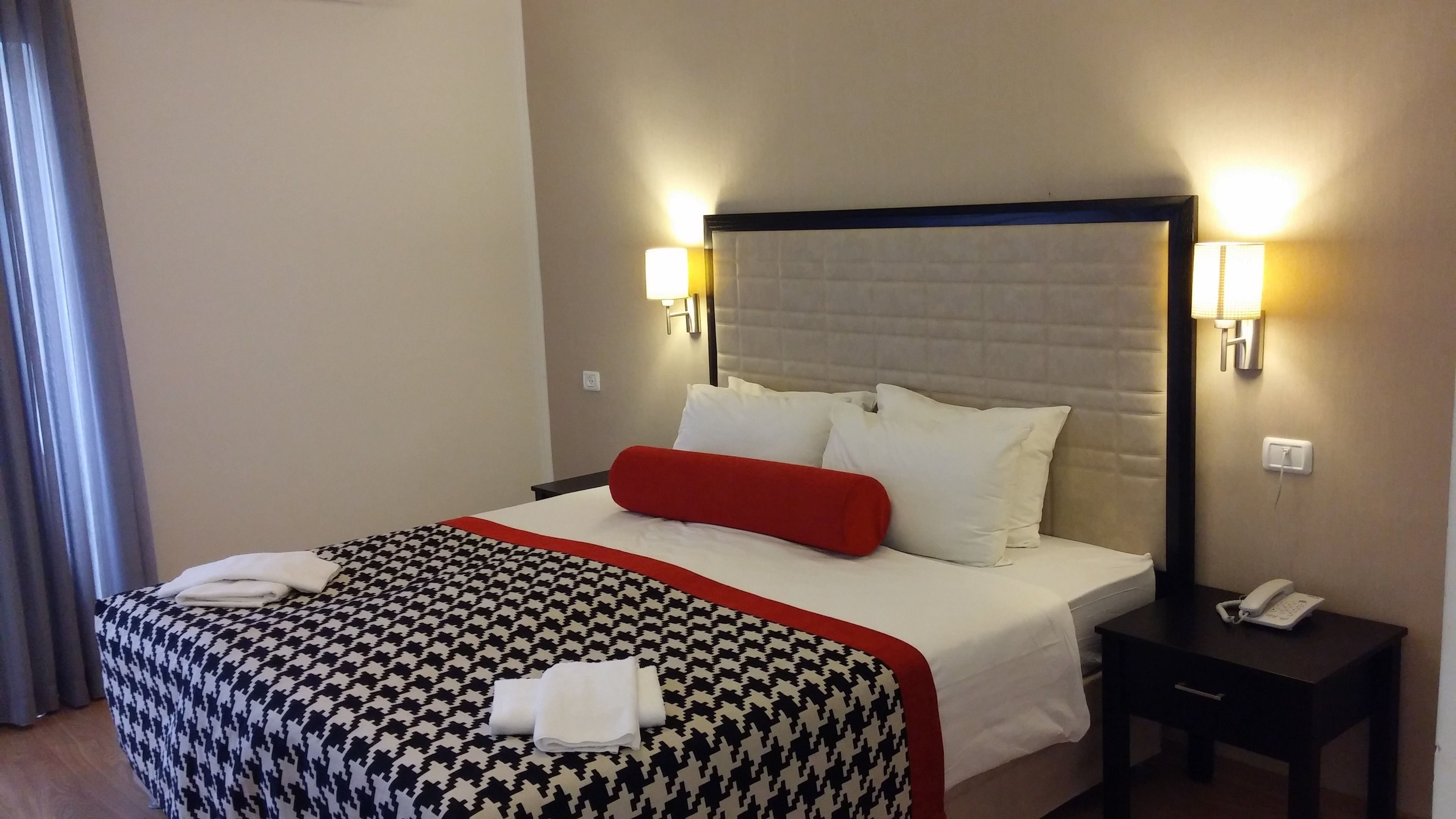 Une chambre d’hôtel avec un grand lit, une table de chevet avec un téléphone et deux lampes fixées au mur.