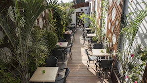 Une terrasse extérieure avec des tables et des chaises, entourée de verdure et agrémentée d’un mur décoratif.