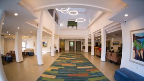 Un hall d’entrée spacieux, agrémenté d’une moquette colorée, de piliers blancs et d’un plafond orné de luminaires circulaires.